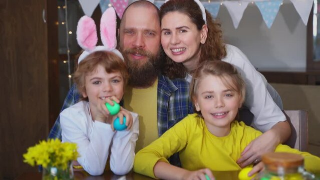 Easter Sunday Family traditions. Parents mom and dad two caucasian happy children with bunny ears posing smiling looking at camera with Easter decorated eggs. Happy family christian holiday