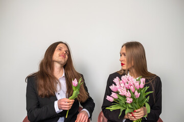 Elegant beautiful couple looking at each other. Woman holding a bouquet of pink tulips. A man...