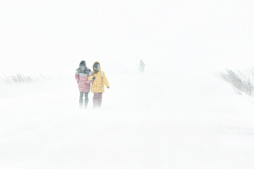 Two girls are walking along the road through a snowstorm in the city, the winter is cold..