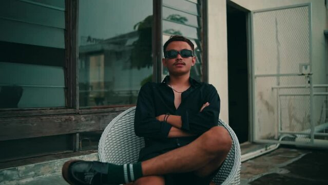Portrait of a young Asian man with sunglasses sitting in a chair outdoors while looking at the camera