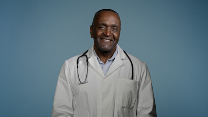 Mature african american man doctor stand in blue background studio in protective mask in medical gown takes off respirator breathe sigh relief breathing deeply feels happy and healthy recovery concept