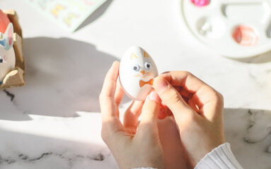 Naklejka premium Hands of caucasian teenage girl in white turtleneck holding easter bunny egg and pasting sticker bow