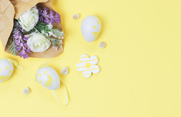 Bouquet of artificial spring flowers in craft paper with willow buds and decorative Easter eggs on a yellow.