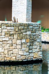 Stone wall with beige white decorative bricks and rocks in afternoon shade near pool or canal in industrial urban area of city