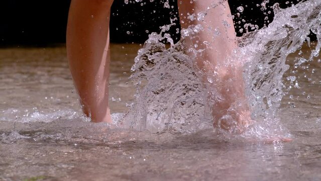 SLOW MOTION, CLOSE UP: Female feet splashing drops while crossing wild river. Enjoyable refreshment in sunny summer days. Splashing spring water while she is crossing pristine river with bare feet.