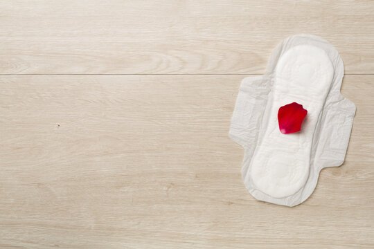 Menstrual pad with red petals on wooden background, top view