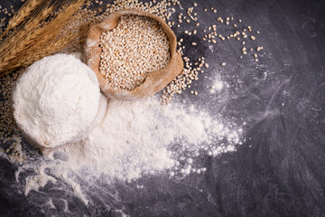 Flour and wheat grains in sacks with wheat ears On a black background table. In a rustic kitchen. Top view.