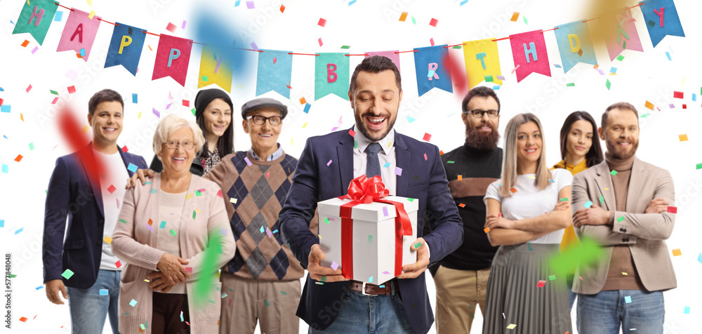 Sticker happy young man in suit and tie holding a present box with red ribbon and people standing behind him