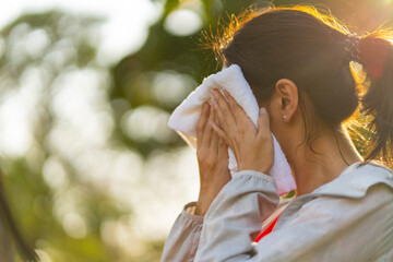 Asian woman in sportswear wiping sweat on her face with towel during jogging exercise at public...