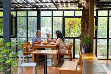 Happy Asian family couple and elderly father having lunch eating food together at cafe restaurant...