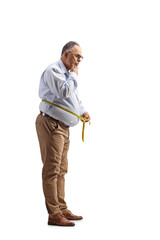 Fototapeta premium Full length shot of a pensive mature man measuring waist with a tape