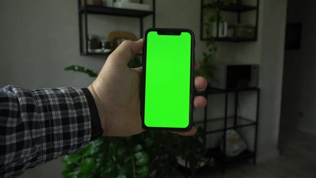 Close up of using smartphone with green screen and scrolling while sitting in room. Mans holding black mobile phone with chroma key in hand, tech concept. Video 4K.