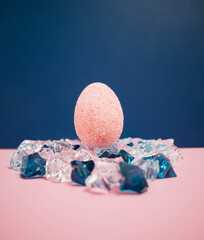 Pink easter egg against dark blue background laying on blue and trasnapernt crystals