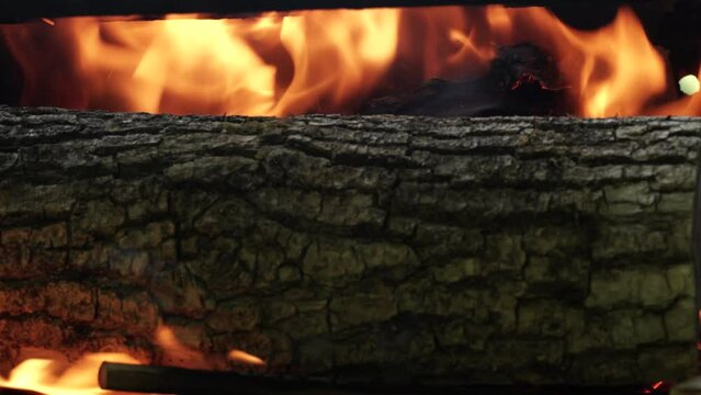 Man put big wood log in grill section for fire. Big fire made for BBQ coals and grilling at summer weekend. Big camp fire close up.