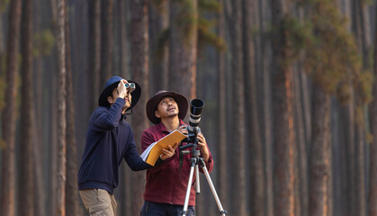 Team of the Asian naturalist looking at the new discovering bird species while exploring in the pine forest for surveying and locating the rare biological diversity and ecologist on the field study - obrazy, fototapety, plakaty