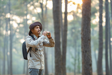 Bird watcher is looking through binoculars while exploring in the pine forest for surveying and...