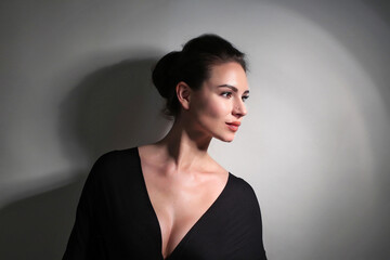 Portrait of a beautiful fashionista brunette girl, with long silver earrings, in black with a neckline on a light white background in the studio room