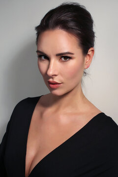 Portrait of a beautiful fashionista brunette girl, with long silver earrings, in black with a neckline on a light white background in the studio room