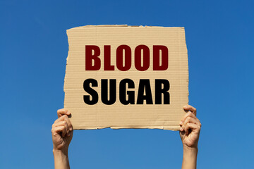 Blood sugar text on box paper held by 2 hands with isolated blue sky background. This message board can be used as business concept about blood sugar.