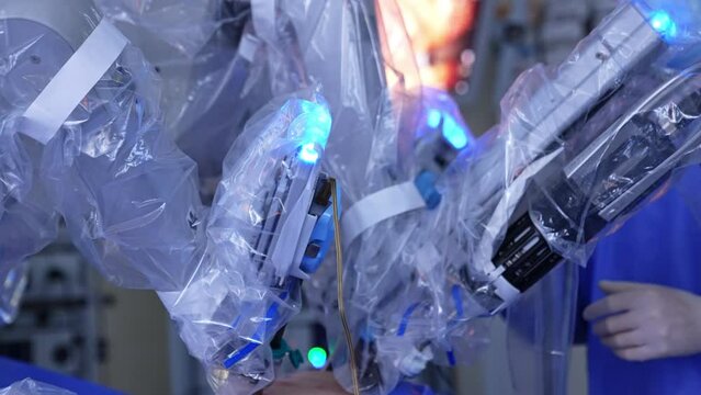 Arms of Da Vinci robot in plastic for sterility move in the operated abdomen. Unknown surgeon stands at backdrop in blur.