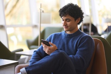 Young Hispanic man using mobile phone, checks social media content, messages. Technology and people