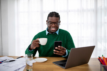 Toothy African American Guy Using Smartphone Having Coffee In Office