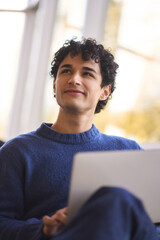 Smiling Latin guy dreamily looking aside, reasoning over his project while works online on laptop