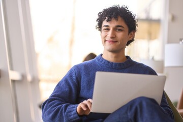 Portrait of a handsome smiling positive Latin American man with laptop looking confidently at camera