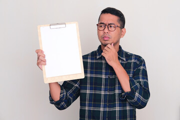Adult Asian man looking to blank white paper on clipboard that he hold with thinking pose
