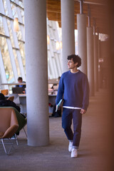 Full length portrait of handsome Latin American student walking on the hall of modern library campus