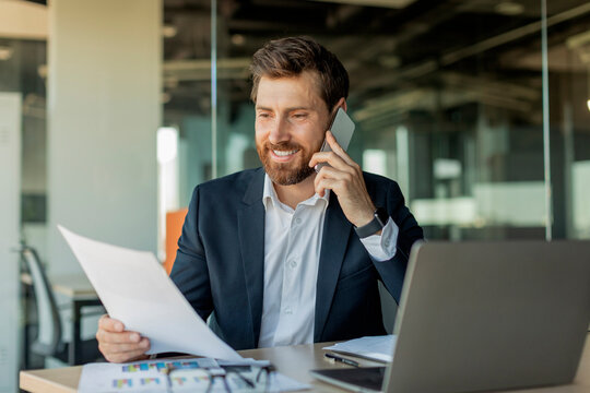 Corporate communication. Happy male manager working remotely, reading financial document and talking on mobile phone