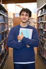 Hispanic young man having free time for hobby and learning, standing in library between bookshelves