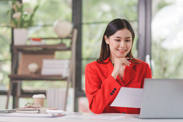 Female attractive asian banker accountant wearing red formal suit calculate the cash bill of audit...