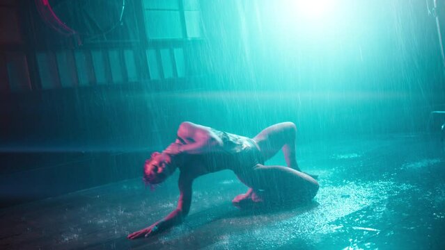 Seductive woman showing sexy body performing striptease on dark cyberpunk urban stage. Hot dancer sitting on wet floor under rain cinematic garage studio background. Professional girl dancer RED shot