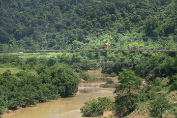 Image of an ethnic minority woman with a red umbrella on a suspension bridge crosses the mountain in Ninh Binh Province, Vietnam