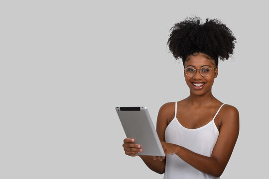  Woman Holding A Tablet Computer, Wearing Glasses Looks At Camera On Gray Background