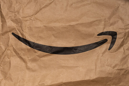 DRESDEN, GERMANY - 23. February 2023: Amazon curved arrow on a packaging. Black smile arrow printed on brown paper. Famous e-commerce logo on a wrinkled background.