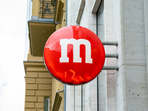 BERLIN, GERMANY - 25. February 2023: Red M dragee sign on a building facade. Advertisement for the m and m's store in Berlin. Chocolate brand of the Mars company. Popular US American sweets.