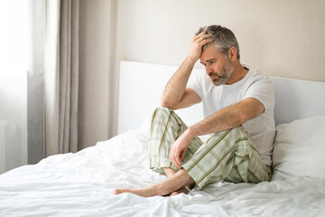 Broken middle aged man sitting on bed in the morning