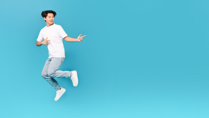 Korean Teen Guy Jumping Pointing Fingers Aside Over Blue Background