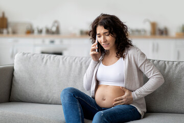 Pregnancy Cramps. Portrait Of Worried Pregnant Woman Touching Belly And Calling Emergency