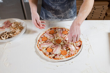 Cooking pizza. Lays out the cheese and salami filling, ingredients on the dough preform. Closeup hand of chef baker in uniform white apron cook at kitchen