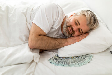 Smiling bearded man sleeping with bunch of cash under pillow