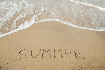Summer 2023 lettering on the beach with wave and clear blue sea. 