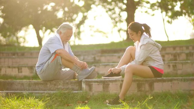 4K Asian woman daughter and elderly father tying running shoe laces before jogging exercise together at park in the city. Retired senior man health care with outdoor lifestyle sport training workout.