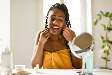 Oral care. Black lady looking in mirror and using dental floss, cleansing teeth, making daily...