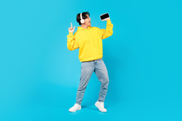 Korean Teen Boy Singing Holding Smartphone Wearing Earphones, Blue Background