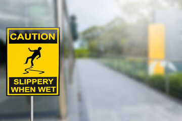 Bright yellow of warning sign on caution slippery when wet  on blurred walk path background.  