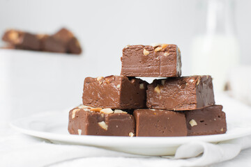 chocolate fudge with nuts on a white ceramic plate, chocolate fudge cut into pieces, fudge candy on a plate