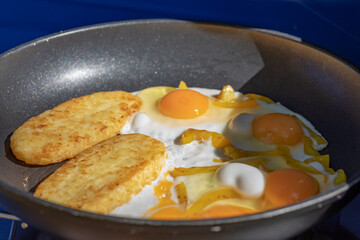 Fried eggs with capsicum and hash browns on a frying pan. Focus in the centre